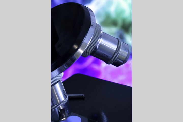 Close up of a microscope in lighting with blues, purples and greens