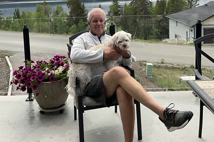 Long-term survivor Roy Vinke and his dog sitting on a deck overlooking mountains and a lake