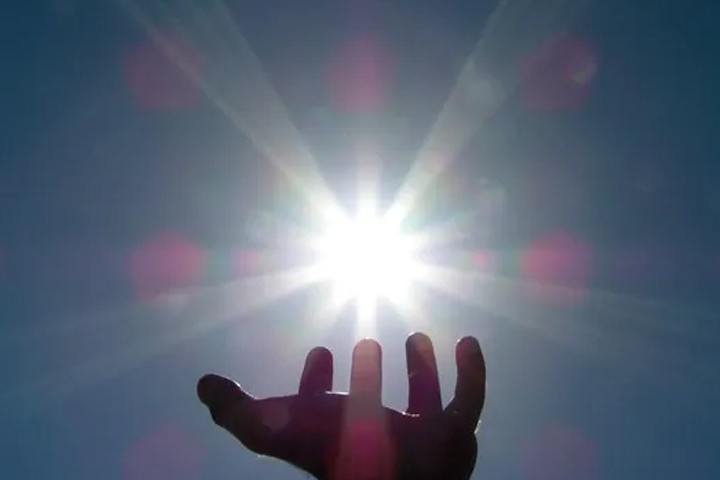 A hand reaching for the sky with the Sun at the center