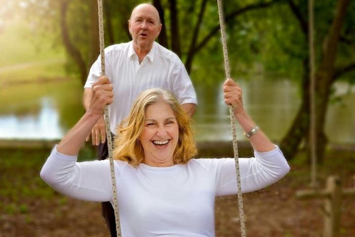 Susan Riddle on a swing, with her husband behind her