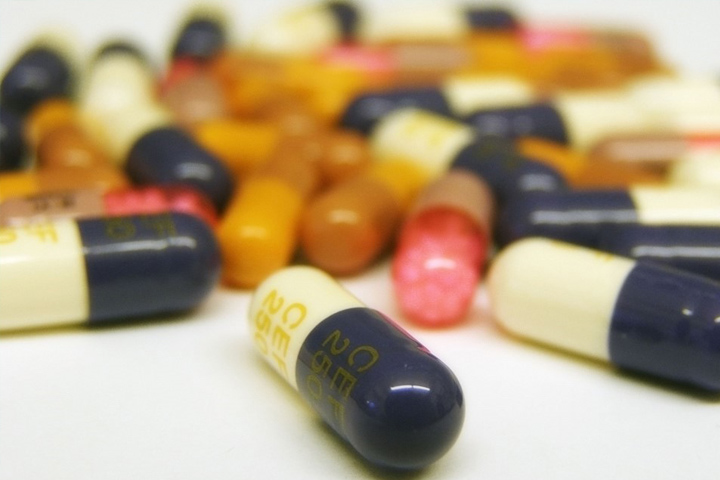 Photo of pill capsules with blue and beige ones in focus in the front, and out of focus pills in brown, pink and brown, and blue and beige in the background