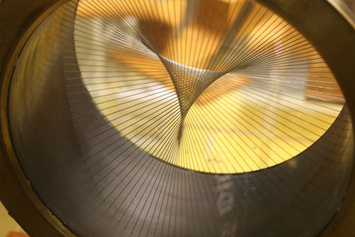 Image of a yellow and gold metal circle with wires across the center, in an abstract geometic pattern.