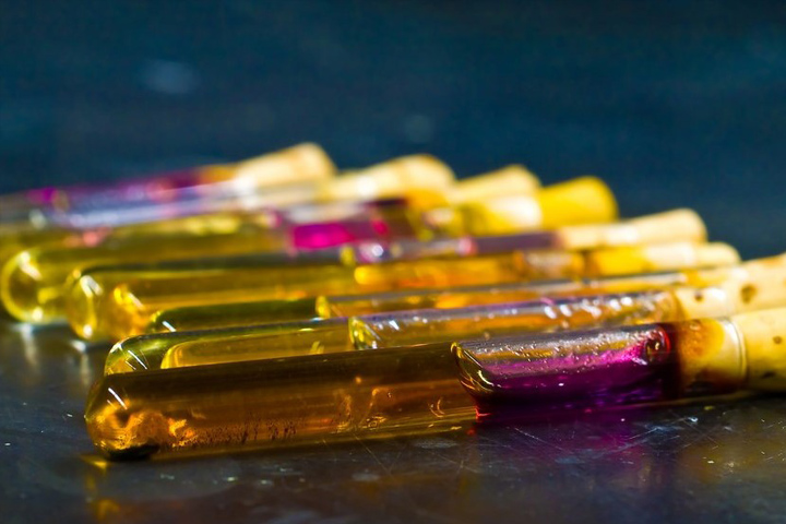 Chemistry test tubes that are capped and filled with yellow and pink liquids, laying flat on a dark blue table