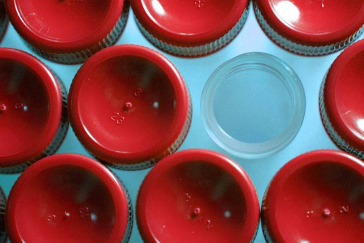 looking down on top of culture test tubes with red tops, against a light blue background