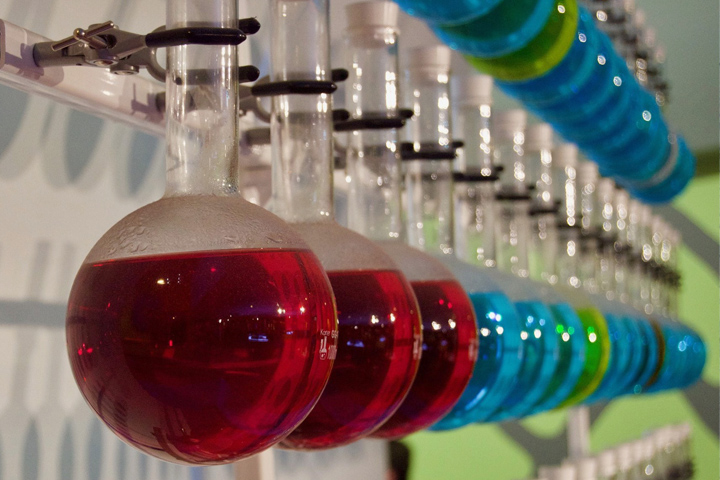 a rack of beakers with red, blue, and green liquids