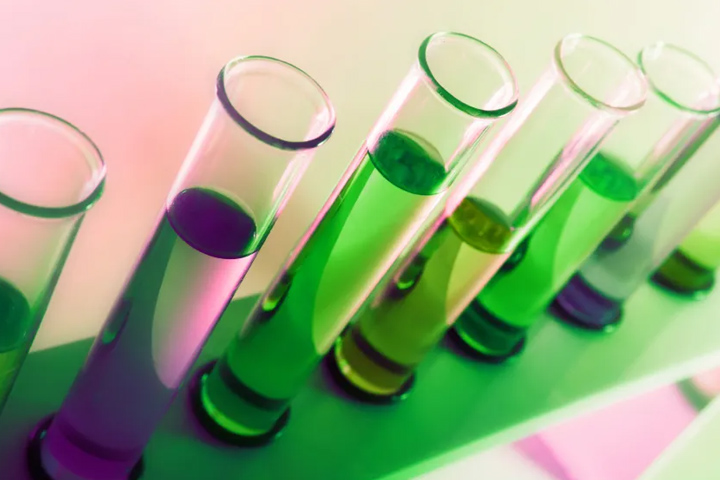 Laboratory test tubes filled with clear liquid and sitting in a rack lit with green and purple lights