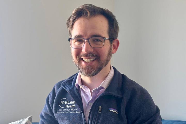 Young man with brown hair, glasses, and a beard, in a pink checked shirt and a blue gray fleece pullover.