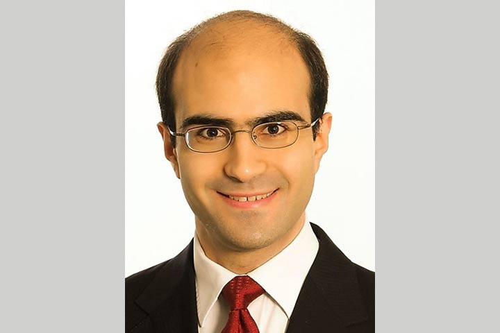 Photo of a bald young man in a suit, white shirt and red tie, with glasses and dark eyebrows