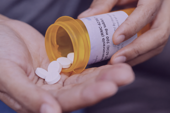 A hand holding white pills from a pill bottle.
