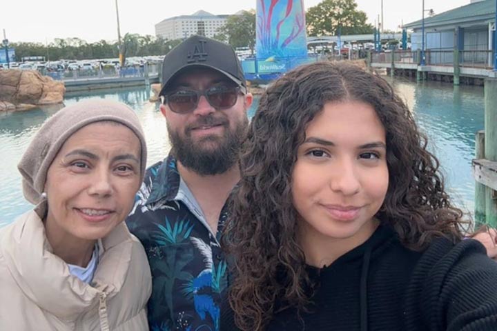 A woman with a scarf on her head, a bearded man in sunglasses and a ball cap, and a young woman with long wavy brown hair.