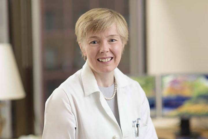 a smiling woman with short blond hair in a doctor's white coat